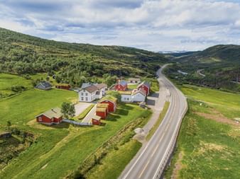 Flyfoto av Kongsvoll Fjeldstue med røde og hvite bygninger ved en vei gjennom den grønne Dovrefjell-dalen i Norge.