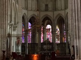 Interior of Gothic cathedral in Chablis with tall stone columns, pointed arches, and colorful stained glass windows illuminating the altar area.