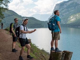 Gruppe vandrere med rygsække på en sti ved siden af en bjergsø, omgivet af dramatiske toppe i Dolomitterne.