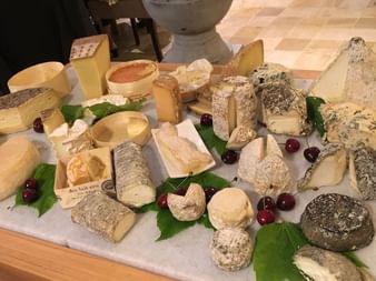 Wooden cheese board with various French cheeses, decorated with green leaves and red cranberries on white paper in Chablis.