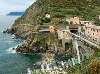 Coastal village in Cinque Terre with colorful buildings on cliffs, stone bridge over rocky coastline, and turquoise Mediterranean waters.