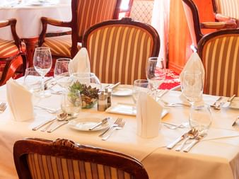 Formelt dækket bord med hvide duge, vinglas og stribede polstrede stole i en krydstogtskibsrestaurant på Donau.