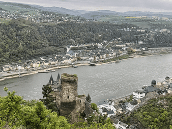 Luftfoto af Rhinen gennem en dal med et middelalderligt slottstårn i forgrunden og byer langs flodbredden.