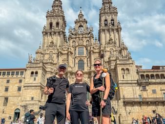 Three hikers posing in front of Santiago de Compostela Cathedral on Portuguese Camino day 14, with ornate baroque towers rising behind them.