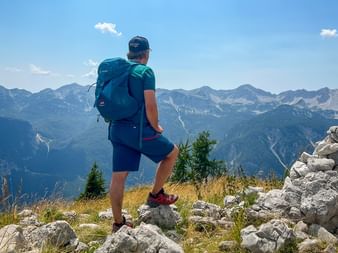 Vandrare med ryggsäck på klippig topp med utsikt över Juliska Alperna i Slovenien under blå himmel med spridda moln.