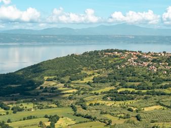 Hilltop village on Via Francigena route overlooking Lake Bolsena with rolling green hills, fields, and mountains in the distance under blue sky.