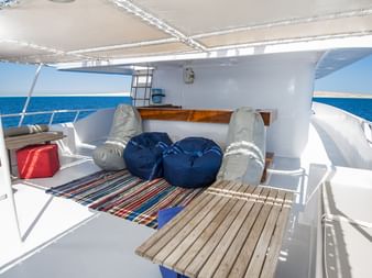 Øvre dæk på MV Tala med hvide polstrede siddepladser, blå sækkestole, stribet tæppe på trægulv, sejldugstelt og havudsigt.