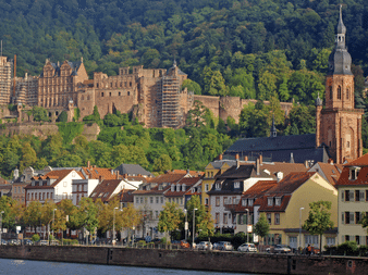 Heidelberg Slots ruiner på en skovklædt bakke over den gamle by med farverige bygninger langs Neckar og et kirketårn.