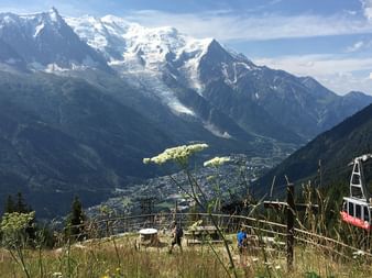 Red and white cable car gondola in foreground with Mont Blanc massif in background, showing snow-capped peaks and glaciers above Chamonix valley.