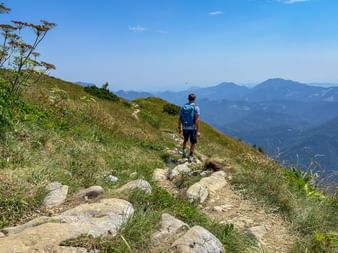 Vandrare med blå ryggsäck på stenig bergsled i Juliska Alperna, Slovenien, med bergskedjor synliga i fjärran.