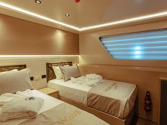 Moderne dobbeltkahyt ombord på High Wave med to enkeltsenge, hvidt sengetøj, træsengegavle, LED-loftslys og koøje.