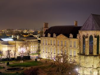 Night view of illuminated historic stone buildings in Champagne, France, featuring Gothic church architecture and classical facades.