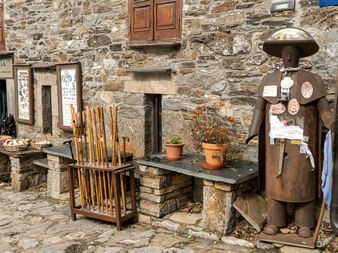 Steinbygning med trebenk, vandrestaver og pilegrimsstatue på Camino de Santiago. Steinmur med vinduer og døråpning.