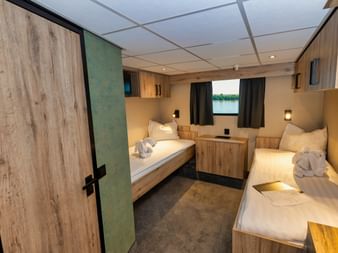 Moderne hoveddæk kahyt på MS PRINCESS med to enkeltsenge, træpaneler, vindue med gardiner og kompakte opbevaringsløsninger.