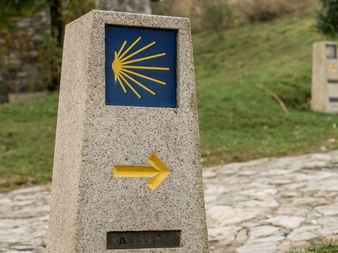 Steinveiskilt på Camino de Santiago med blå flis som viser gult pilegrimsskjellsymbol og gul retningspil på brostein.