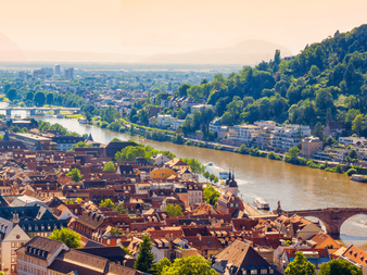Luftfoto af Heidelberg med rødtaget gammel by, Neckar, historisk stenbro og skovklædt bakke med slotsruin.