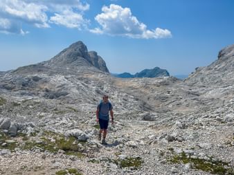 Vandrare på stenig kalkstensmark i Juliska Alperna med dramatiska bergstoppar under blå himmel med vita moln.