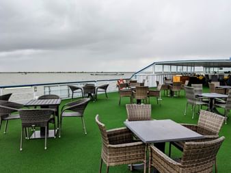 Soldæk på MS Rigoletto med kurvmøbler på grønt kunstgræs. Flod og skyet himmel synlig i baggrunden.