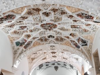 Utarbeidet malt tak med geometriske paneler som inneholder religiøse scener og dekorative motiver i hvitt hvelvd kirkeinteriør.
