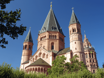 Strasbourg Domkirke med lyserød sandstenfacade og flere tårne med grønne tage mod blå himmel, indrammet af grønne træer.