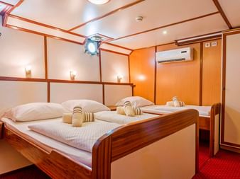 Interiør af MS Amore skibskahyt med to enkeltsenge, træpaneler, koøjer, aircondition og rødt tæppe på gulvet.