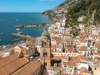 Aerial view of a Cinque Terre village with colorful houses, church bell tower, and small harbor on the Mediterranean coast.