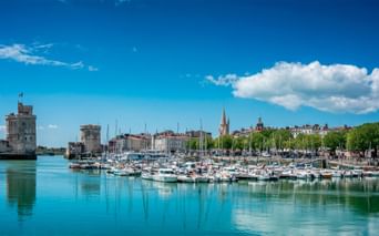 Marina i La Rochelle med talrige hvide sejlbåde fortøjet i roligt turkist vand. Middelalderlige stentårne vogter havneindgangen.