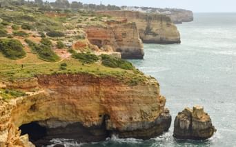 Gyldne kalkstensklipper langs Algarvekysten mellem Lagos og Tavira med grøn vegetation på toppen og turkisblåt havvand nedenfor.