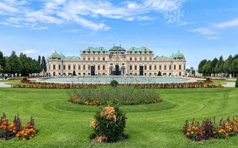 Øvre Belvedere i Wien med grønne kobberkupler, symmetrisk barokfacade og velholdte haver med farverige blomsterbede.