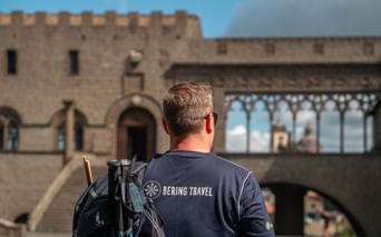 Hiker with backpack viewing medieval stone buildings with crenellated walls and arched openings in Orvieto on the Via Francigena route.