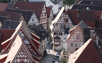 Luftfoto af traditionelle bindingsværkshuse med røde og brune tage i Bad Wimpfen, Tyskland. En smal gade løber mellem de historiske bygninger.