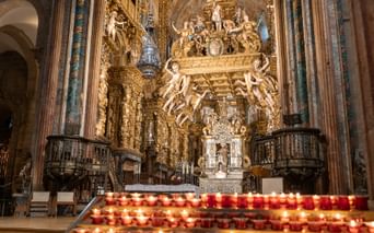 Interiør af Santiago de Compostela katedral med udsmykket barok alter med gyldne dekorationer og rækker af tændte bønelys.