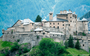 Château Queyras, en middelalderborg med stenmure og tårne, på en bakke i Ville-Vieille med skovklædte bjerge bagved.