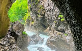 Udsigt fra en klippefyldt kløft nær Zugspitze med turkisblåt vand mellem mosdækkede klipper og grøn skov ovenover.
