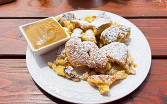 Austrian Kaiserschmarrn dusted with powdered sugar on a white plate, served with applesauce in a small bowl on a rustic wooden table.