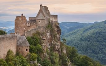 Middelalderlig stenburg på en klippefyldt klippe i Wachau-dalen, Østrig, med skovklædte bakker og Donau synlig i baggrunden.