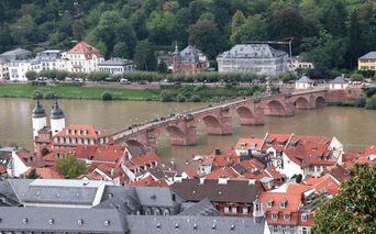 Historisk stenbro over Neckar i Heidelberg, med rødtagede gamle bygninge og kirketårne i forgrunden.