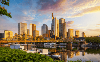 Frankfurt am Mains skyline med moderne skyskrabere reflekteret i Main. Gul jernbro krydser vandet, både fortøjet langs bredden.