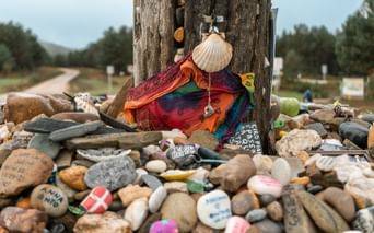 Trestolpe med pilegrimsskjell og fargerikt stoff omgitt av hundrevis av malte steiner etterlatt av Camino-pilgrimer.