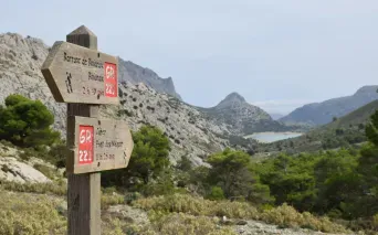 Tre-skilt for turstier med røde markeringer som viser retninger til forskjellige destinasjoner i steinete middelhavs-landskap.