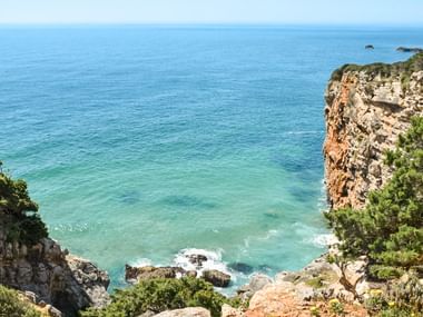 Dramatiske klippeskrænter dækket af grøn vegetation med udsigt over turkisblåt vand langs Algarvekysten mellem Lagos og Tavira, Portugal.
