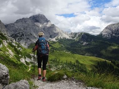Fotturist med ryggsekk og vandrestaver på fjellsti i Dachstein-regionen, Østerrike. Dramatiske kalksteinstopper og grønne daler synlige.