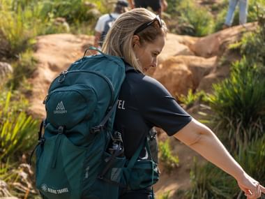 Kvindelig vandrer med turkis Gregory-rygsæk navigerer klippefyldt terræn i Sri Lanka, omgivet af frodig grøn vegetation.
