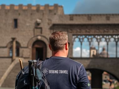 Vandrer med rygsæk betragter middelalderlige stenbygninger med tinder og buer i Orvieto på Via Francigena.