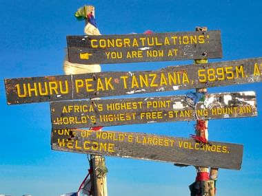 Uhuru Peak Kilimanjaro toppskilt på 5895m Træskilt ved Uhuru Peak, Kilimanjaro med tillykke-besked og højde på 5895m, Afrikas højeste punkt.