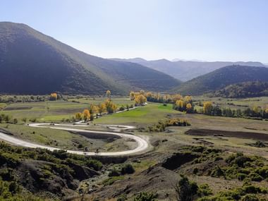 Svingete vei gjennom en grønn dal i sør-Albania, omgitt av åser og fjell under en klar blå himmel.