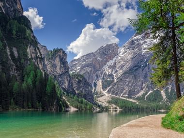 Pittoresk bergsjö i Dolomitterna med turkost vatten, omgiven av dramatiska kalkstenstoppar och grön skog under blå himmel.
