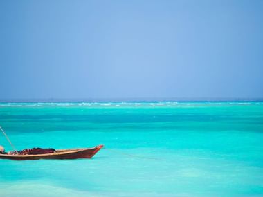 Traditionel båd i turkise farvande En traditionel træfiskerbåd forankret i krystalklart turkist vand ud for Zanzibar under en klar blå himmel.