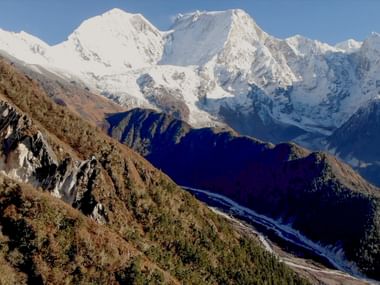 Panoramautsikt över snötäckta Manaslu-toppar i Nepal med klippiga sluttningar i förgrunden och djupblå dalar nedanför.