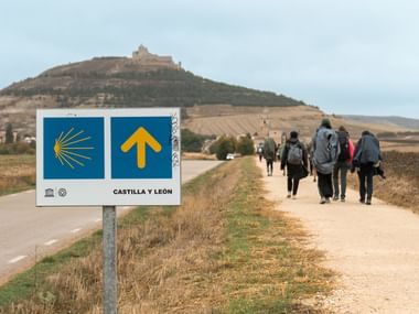 Gruppe pilgrimme der vandrer på Camino de Santiago med Castilla y León vejskilt med gul pil og muslingesymbol.